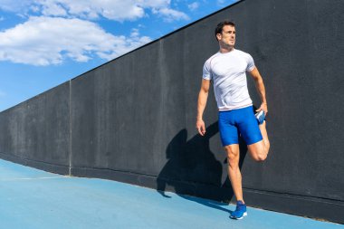 Mavi pantolonlu ve beyaz gömlekli genç adam dinleniyor ve güneşin altında siyah duvarda iyileşiyor, bacak esneme hareketleri yapıyor. Motivasyon konsepti, kariyer