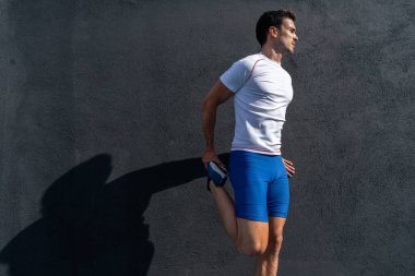 Mavi pantolonlu ve beyaz gömlekli genç adam dinleniyor ve güneşin altında siyah duvarda iyileşiyor, bacak esneme hareketleri yapıyor. Motivasyon konsepti, kariyer