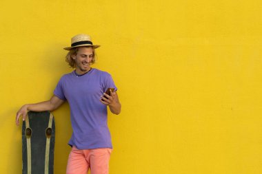 Yazlık kıyafetleri, şapkası ve güneş gözlükleriyle genç sarışın adam yazın tadını çıkarıyor ve cep telefonuyla konuşuyor.