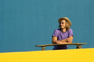 Kaykaylı, şapkalı ve güneş gözlüklü sarışın genç adam yazın tadını çıkarıyor.