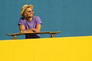 Kaykaylı, şapkalı ve güneş gözlüklü sarışın genç adam yazın tadını çıkarıyor.