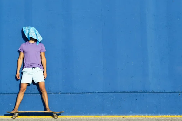 Young blond man with blue scarf on top of a skate with a blue background. Summer, surf concept.