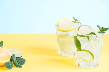 Limonlu iki bardak limonata ve naneli ve buzlu mojito kokteyli. Sarı arka planda fotokopi alanı var.