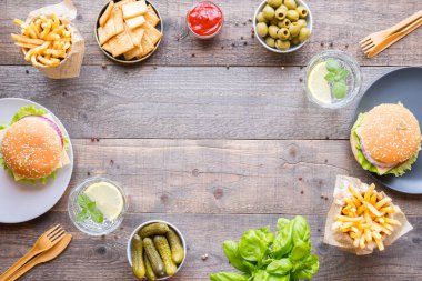 Hamburger, patates kızartması, sebze, sos, abur cubur ve ahşap arka planda limonata. Salgından sonraki sosyal mesafe, kopyalama alanı.