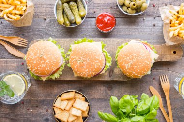 Hamburger, patates kızartması, sebze, sos, abur cubur ve ahşap arka planda limonata..