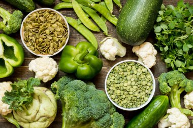 Yeşil ve mor sebzelerden oluşan üst manzara ve koyu ahşap zemin üzerine yayılmış vejetaryenler için protein.