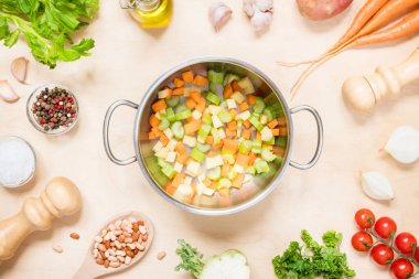 Bir tencerenin üst görüntüsü ve sebze çorbası yapmak için çeşitli taze çiğ sebze malzemeleri.