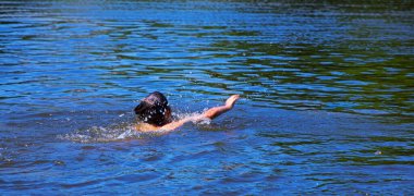 Mutlu çocuk mavi gölde sürünmeyi öğreniyor, tatiller, yaz deneyimleri, rahatlama, doğal arka plan