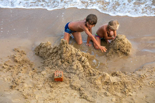 happy children play with sand by the sea on the beach on a summer day, horizontal format