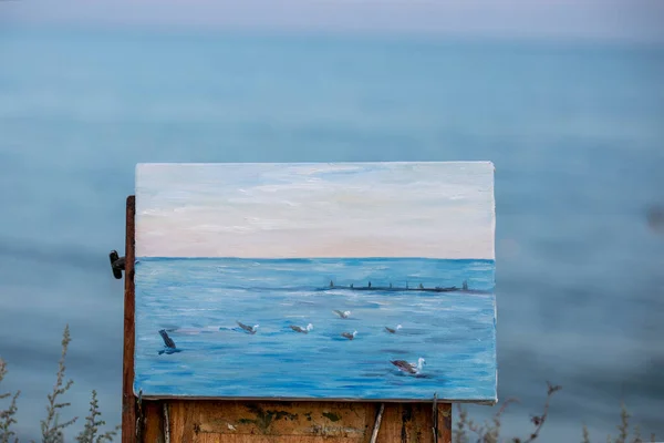 sketch evening sea with seagulls painted in oil paints on canvas, on an easel against the background of the sea, horizontal format
