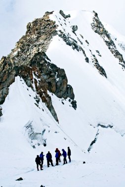 Bir grup dağcı, karlı bir uçurumun kenarında, Elbrus akşam bulutlarına tırmanıyor, 4000 metre yükseklikte.