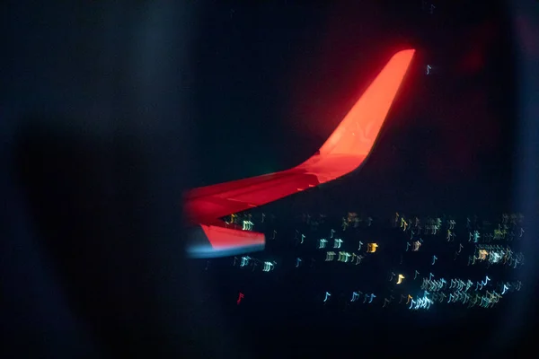 从夜间城市的飞机上看 红色的尾翼模糊了水平线 — 图库照片