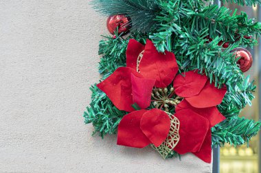 Ortasında kırmızı bir çiçek olan Noel çelengi duvarın yanındaki kapıda. Yeni yıl için dekorasyon ve hazırlık