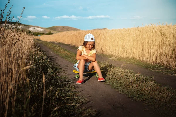 Egy Farmer Kezeslábasban Ülő Kislány Egy Gördeszkán Egy Búzamező Közepén — Stock Fotó