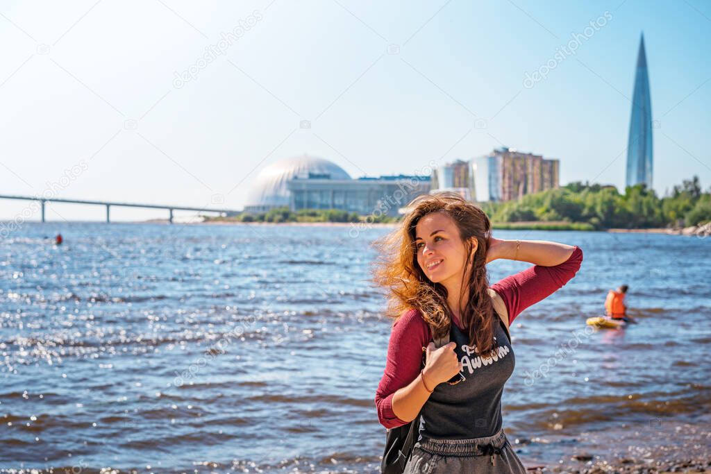 A girl on the beach by the sea of the Gulf of Finland in St. Petersburg with a view of the Lakhta Center skyscraper