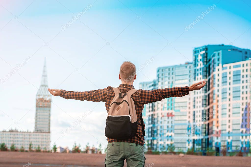 A happy young man in a checked shirt spread his arms in the sky against the background of multi-colored multi-storey new buildings, happiness from buying real estate