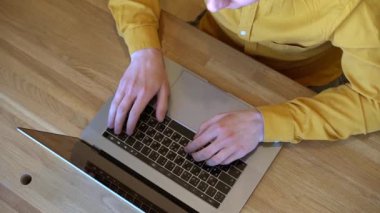 Sarı tişörtlü genç programcı, tahta bir masada oturuyor ve klavyesinde daktilo kodları yazıyor.