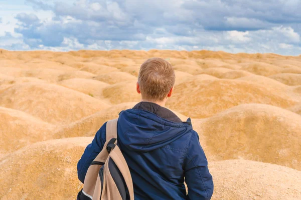 身材矮小的金发男子背着背包 背对着镜头站在沙漠中形状怪异的沙丘上 — 图库照片