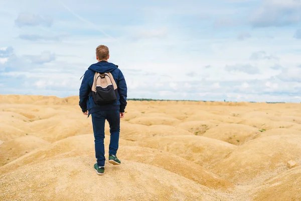 身材矮小的金发男子背着背包 背对着镜头站在沙漠中形状怪异的沙丘上 — 图库照片