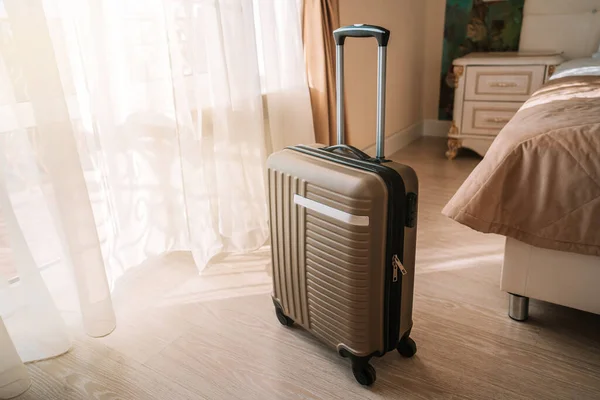 Travel suitcase stands in a white clean hotel room with light from the window, relaxing time, holiday, weekend and traveling concept.