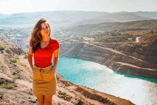 A beautiful woman in red clothes stands over a quarry with an azure lake, Kadykovsky quarry is a tourist natural attraction