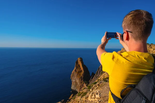 Молодой Человек Рюкзаком Фотографирует Смартфона Вид Скалы Синее Море — стоковое фото
