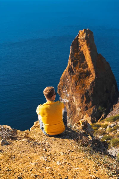 Молодой Человек Жёлтой Одежде Сидит Высоко Над Морем Фоне Прибрежных — стоковое фото