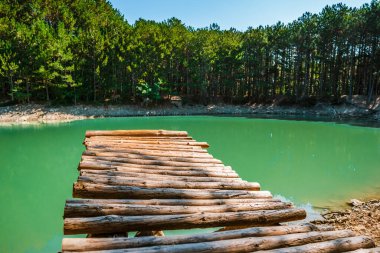 Panoramic view of an extraordinary mountain lake of emerald color in the Crimea, a wooden bridge protrudes above the water clipart
