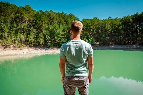 一个金发碧眼的男人背对着摄像机站在森林里一个碧绿的山湖前 — 图库照片