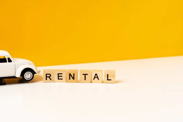 Toy white car on a white table with a yellow background, the inscription of wooden blocks. The concept of a rental car and car sharing.