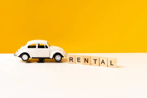 Toy white car on a white table with a yellow background, the inscription of wooden blocks. The concept of a rental car and car sharing.