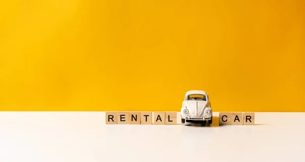 Toy white car on a white table with a yellow background, the inscription of wooden blocks. The concept of a rental car and car sharing.