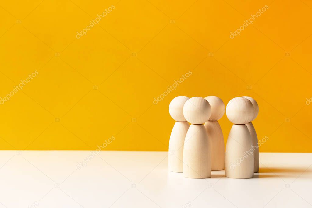 Company of wooden people on a yellow background with letters. The concept of team work and management, copy space