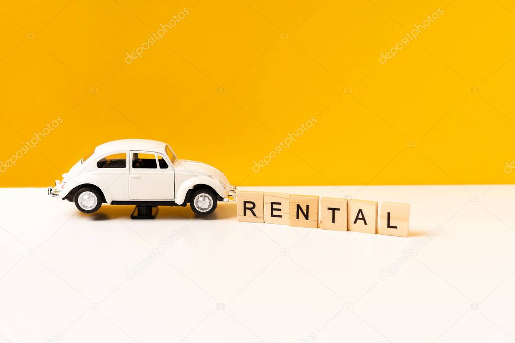 Toy white car on a white table with a yellow background, the inscription of wooden blocks. The concept of a rental car and car sharing.