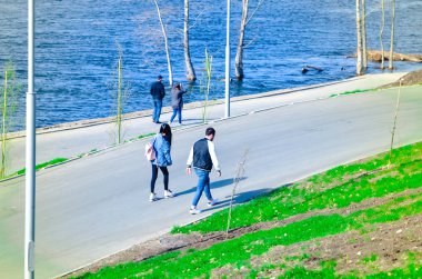 gezinti yolu boyunca yürüyen insanlar, Bisiklet ve scooter, nehir veya deniz akan su izlerken 