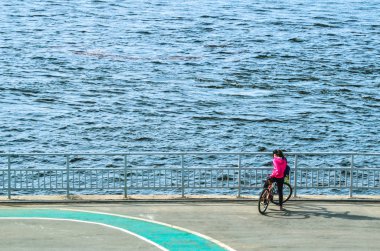 gezinti yolu boyunca yürüyen insanlar, Bisiklet ve scooter, nehir veya deniz akan su izlerken 