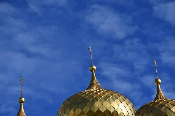 Golden domes with a cross on the background of blue sky and clouds.