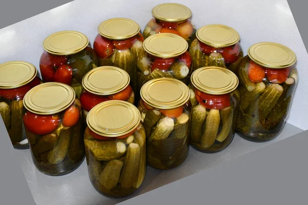 Home canning. Glass jars with salted or pickled cucumbers and tomatoes. Spices and spicy herbs are laid on the bottom of the jar. The jars are covered with yellow metal covers. Glare of light.