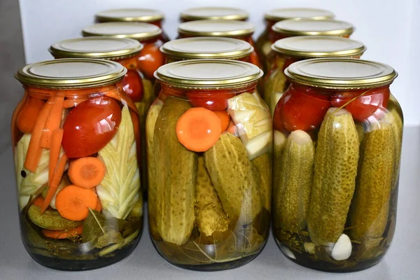 Home canning. Glass jars with salted or pickled cucumbers, tomatoes, carrots and zucchini. Spices and spicy herbs are laid at the bottom of the jar. The jars are covered with yellow metal covers.