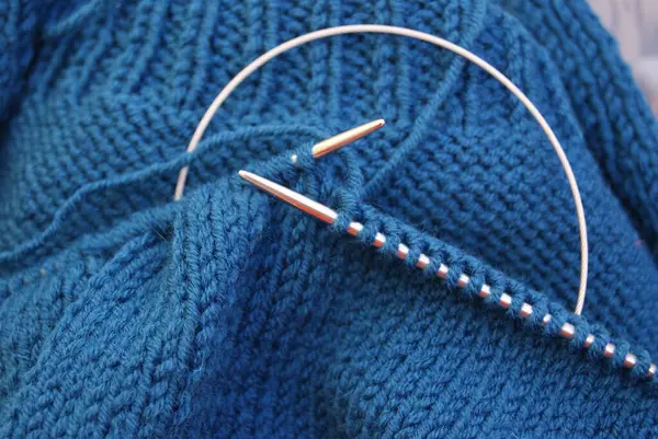 Knitting needles in the process of knitting from blue wool yarn