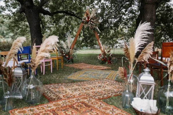 Düğün törenini boho tarzında ziyaret etmek. Çiçeklerle süslenmiş üçgen ahşap kemer..