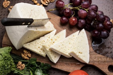 Tahtada üç köşeli peynir dilimleri. Etrafta bir sürü sebze ve üzüm var. Üstten yakından bak. Gürcistan mutfağı