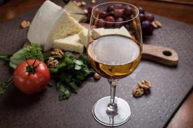 Bir kadeh beyaz şarap yakın plan. Peynir ve sebzeler arka plandaki bir tahtada dilimlenir. Gürcistan mutfağı