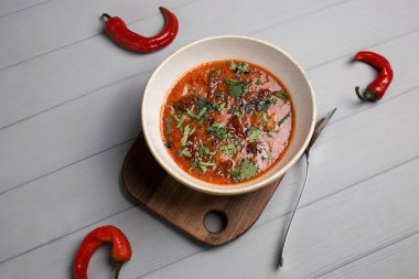 Bir tabak çorba, bir kaşık ve bir el. Kırmızı biber etrafa saçılmış. gri ahşap arkaplan