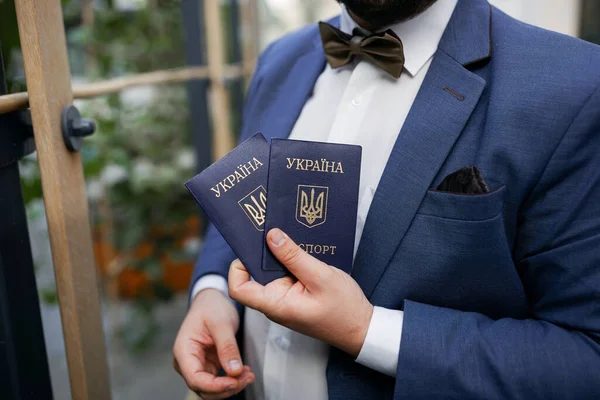 Mavi takım elbiseli ve papyonlu bir adam elinde iki Ukrayna pasaportu tutuyor. Ukraynalıların göçü.