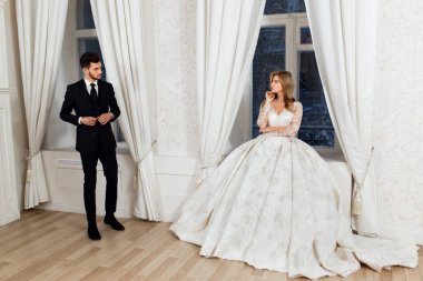  Gelin ve damat bir ışık stüdyosunda antik ayna ve pencerenin yanında duruyorlar..