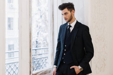 Bir fotoğraf stüdyosunda siyah takım elbiseli damat. Pencerenin yanında poz veriyor. Şık düğün.