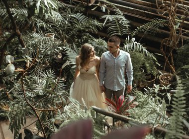 Botanik bahçesinde poz veren genç bir çift. Tropikal bitkilerle düğün fotoğrafı çekimi.