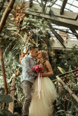 Botanik bahçesinde poz veren genç bir çift. Tropikal bitkilerle düğün fotoğrafı çekimi.