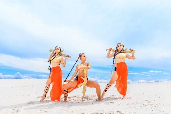 女孩们穿着红色的裙子 手里拿着金色的机器 在海滩上跳舞 白沙蓝天 — 图库照片
